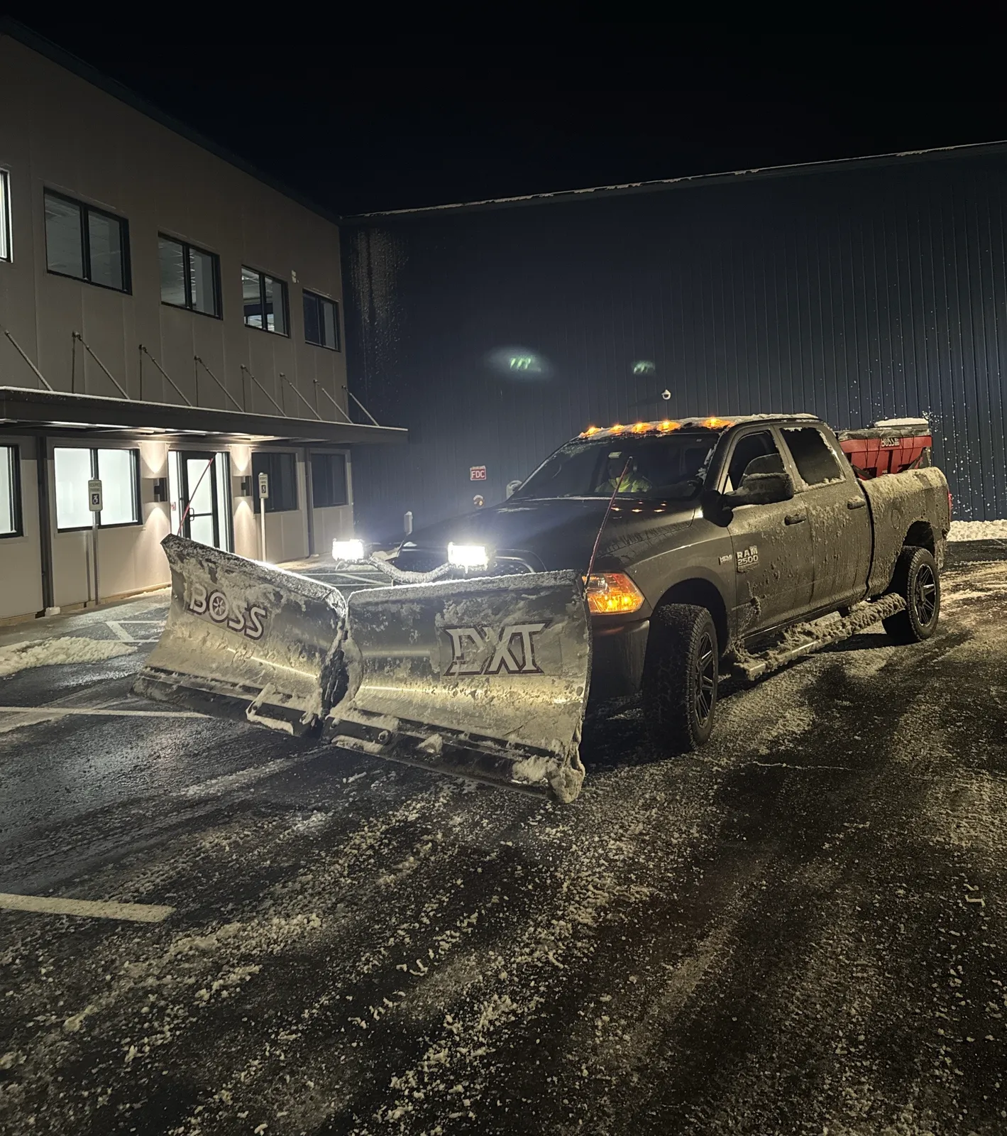 Snow plow truck clearing a lot at night